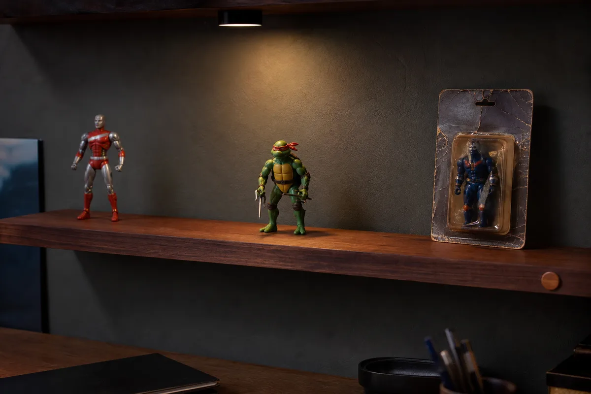 Étagère murale étroite au-dessus d’un bureau, trois figurines rétro espacées et éclairage LED discret