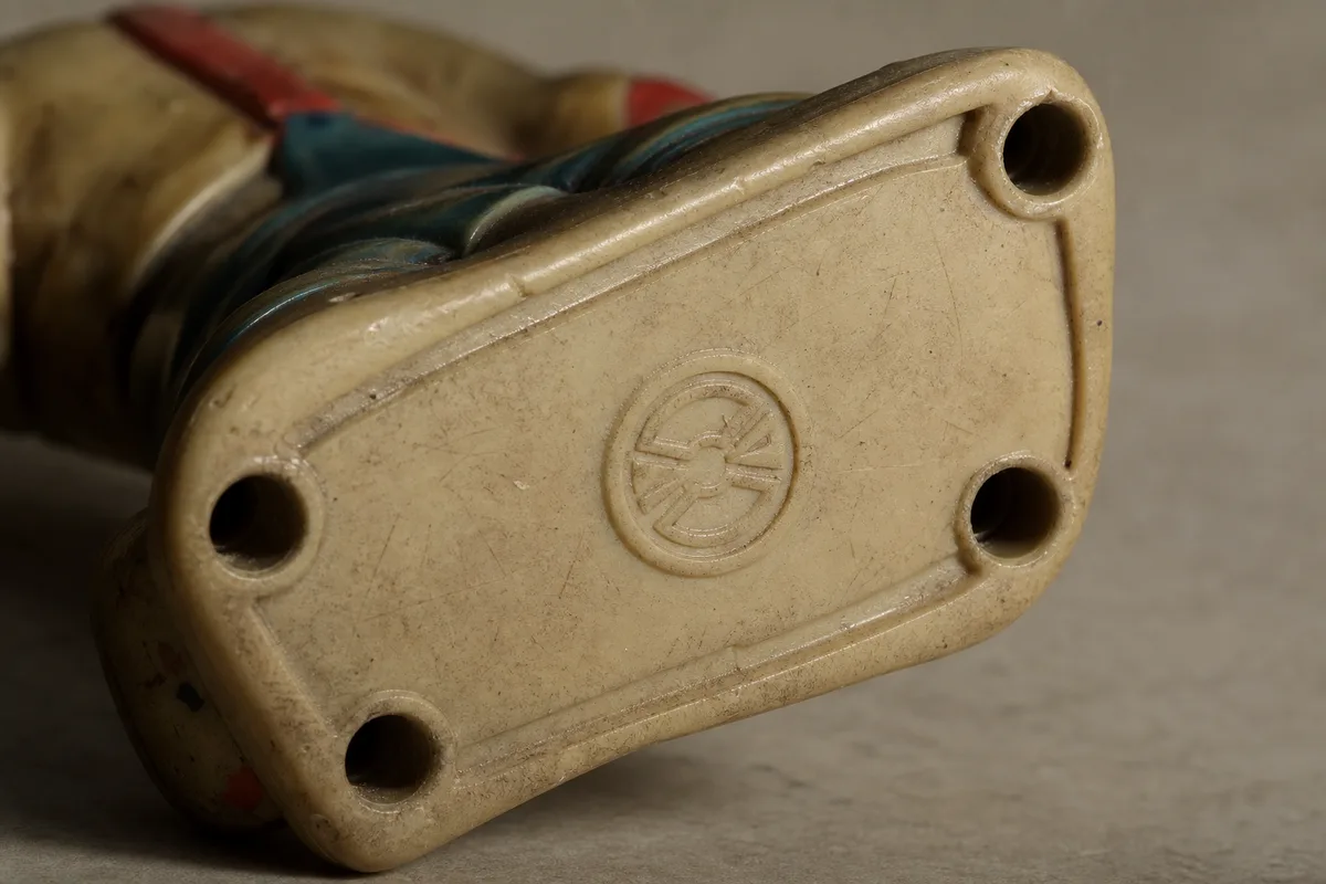 Gros plan sur le dessous d&rsquo;une figurine ancienne révélant un marquage moulé et un numéro de série