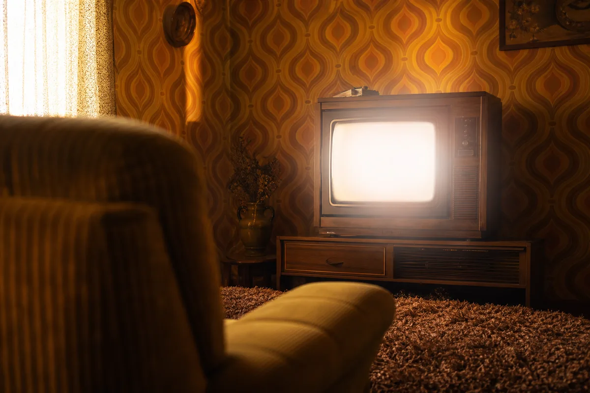Poste de télévision cathodique des années 70 allumé dans un salon au papier peint orangé