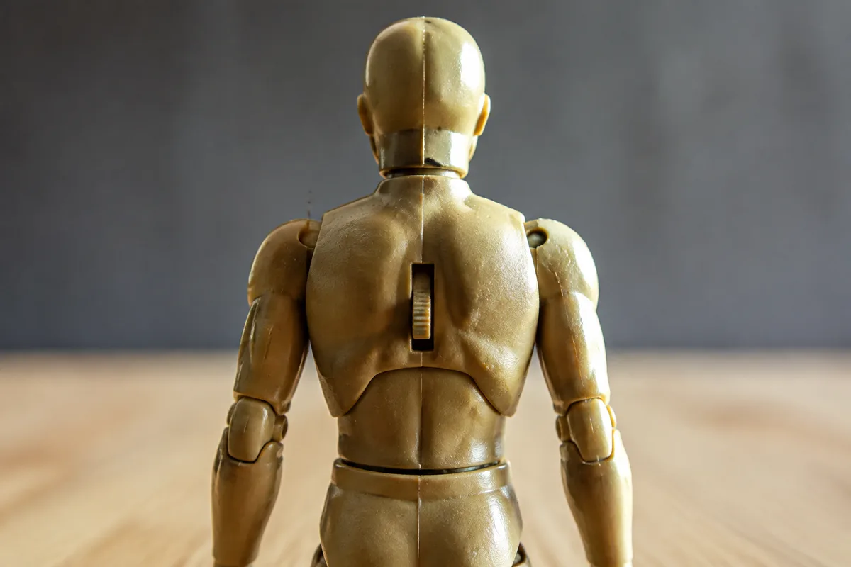Figurine articulée générique en plastique vue de dos, levier d&rsquo;action visible entre les omoplates, lumière rasante d&rsquo;atelier
