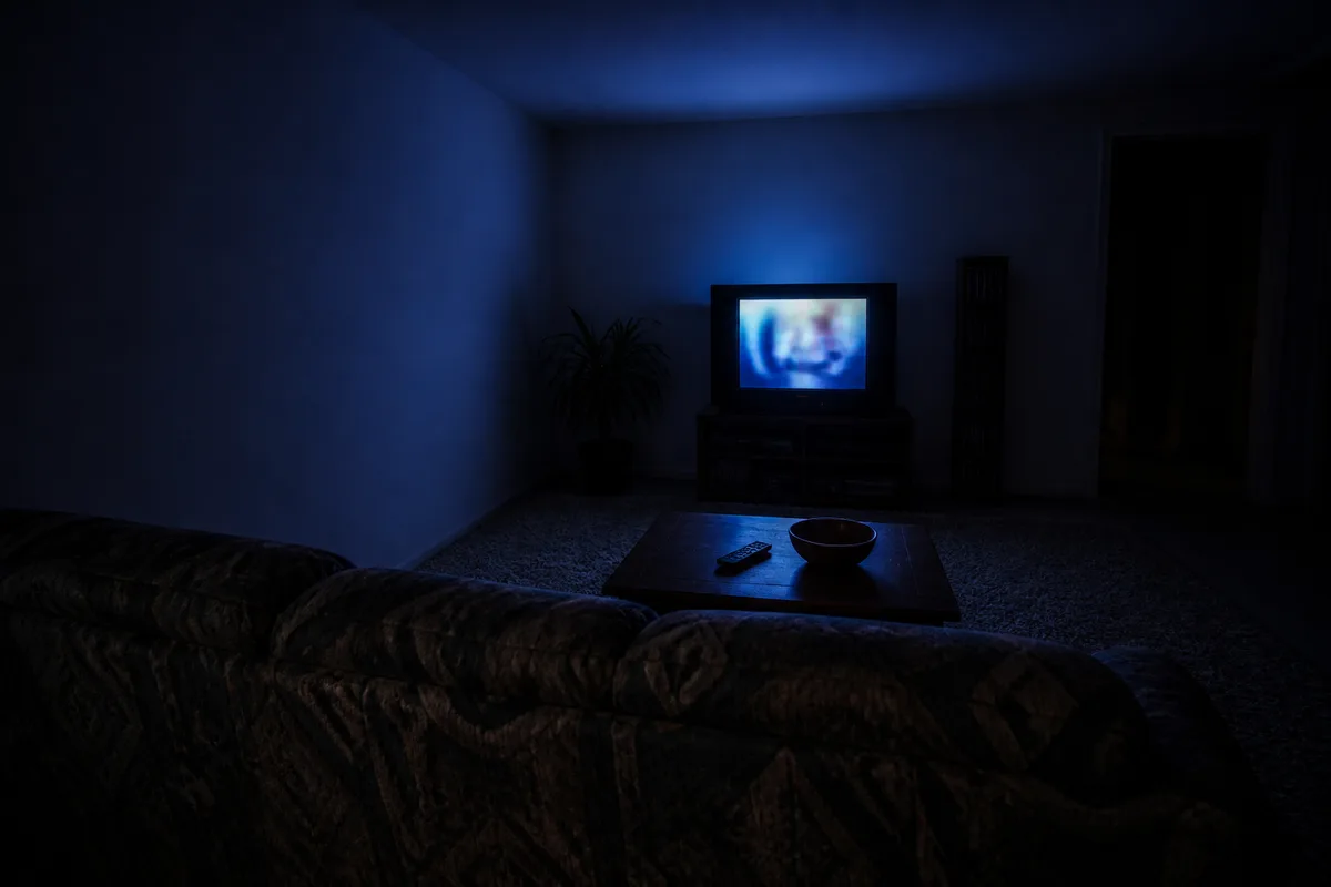 Salon familial vide de nuit, canapé à motifs et téléviseur cathodique allumé projetant une lueur bleutée
