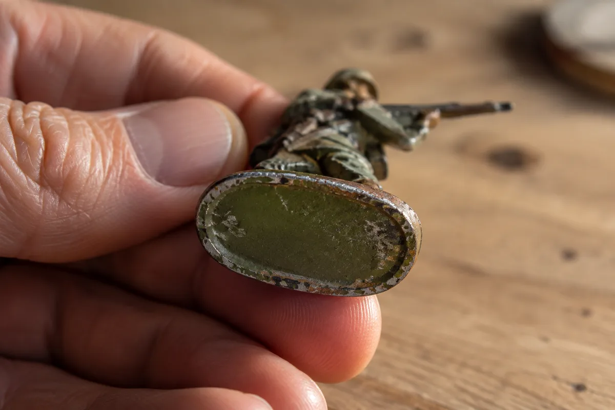 Dessous du socle ovale d’une petite figurine militaire ancienne éclairé en lumière rasante